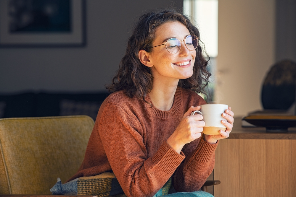 A cheerful woman with glasses smiles while holding a cup of coffee, representing comfort and confidence after dental care – Root Canal Cerritos.