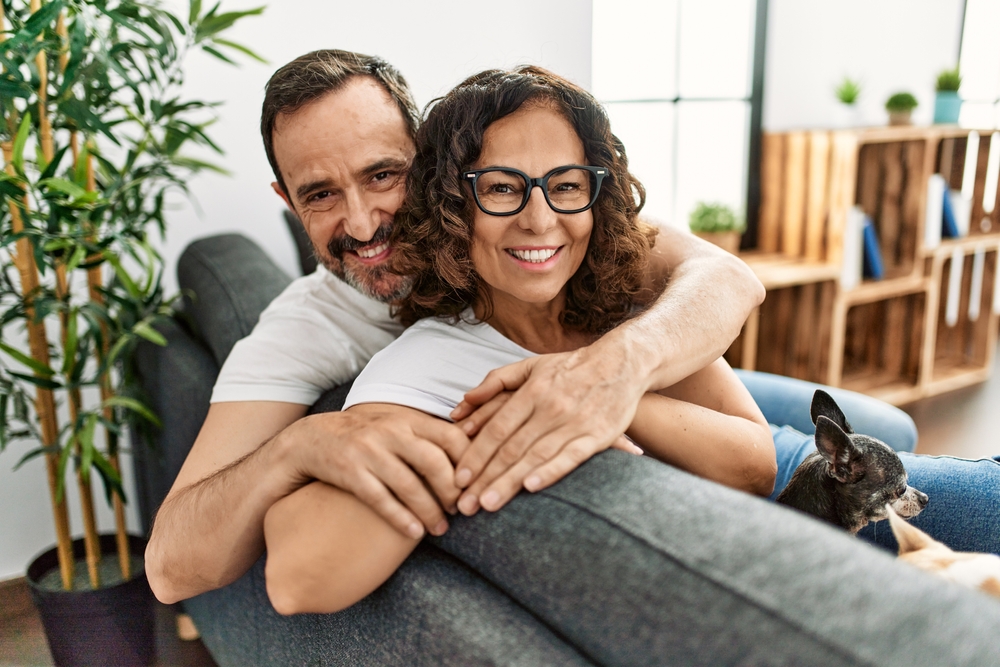 Happy couple relaxing together at home – Root Canal Therapy in Long Beach CA A smiling couple embraces while relaxing on their couch with their dog, representing comfort and confidence after treatment – Root Canal Therapy in Long Beach CA.