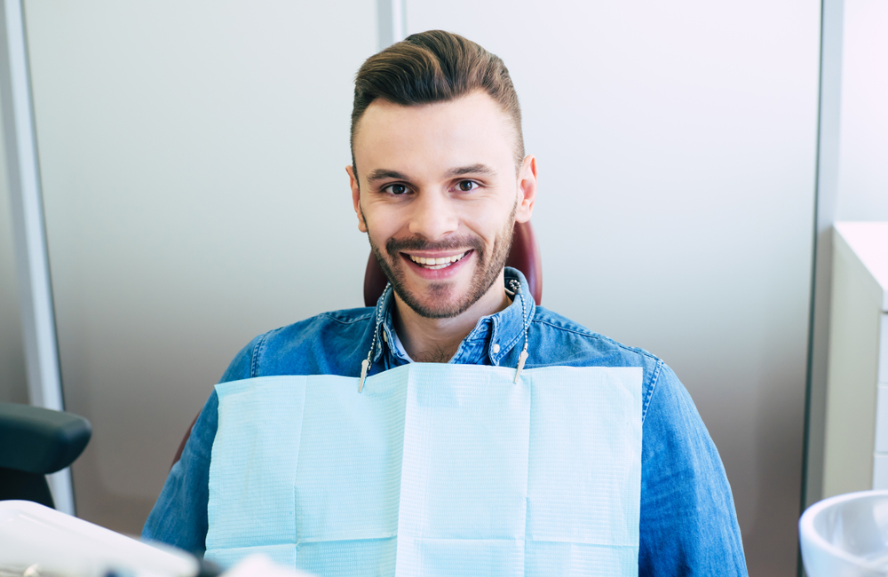 Smiling man sitting in dental chair after treatment – Root Canal Treatment A young man sits comfortably in the dental chair, smiling confidently after a successful procedure – Root Canal Treatment.
