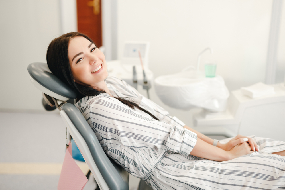 A cheerful woman relaxes in a dental chair, showing satisfaction and comfort after professional endodontic treatment – Endodontist Long Beach.
