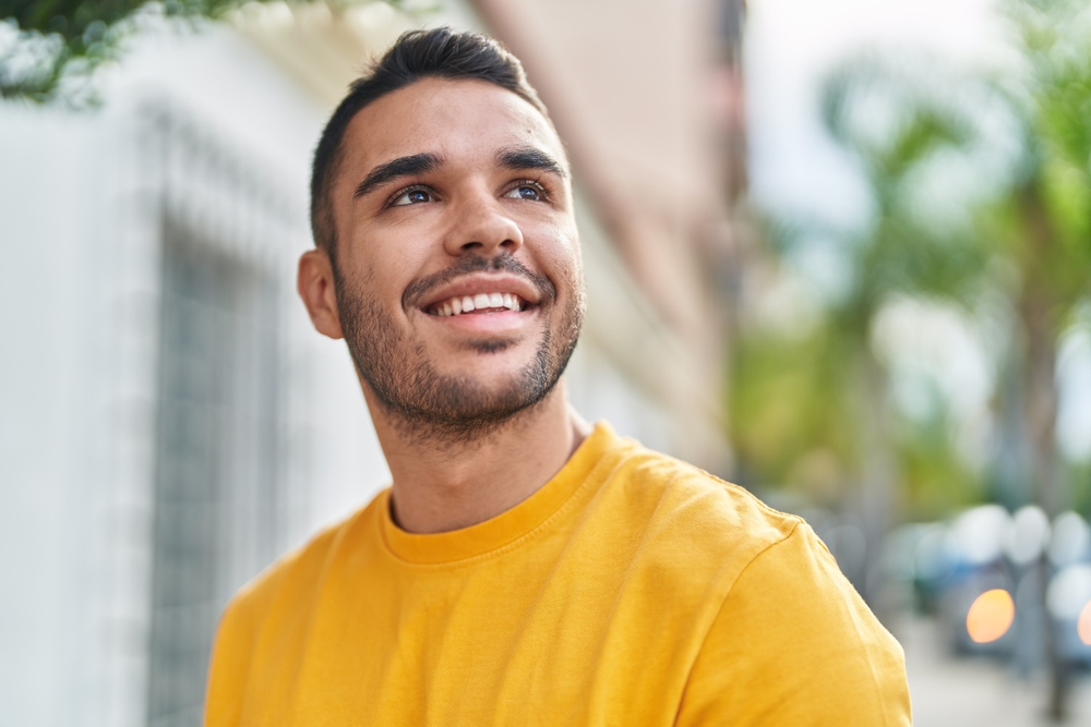 Confident man smiling outdoors with bright, healthy teeth – CBCT A cheerful young man in a yellow shirt smiles confidently outside, showcasing excellent dental health made possible through accurate CBCT imaging and professional care.