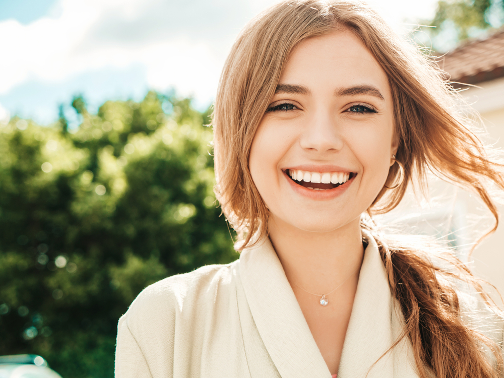 Young woman smiling outdoors in natural light – Non-Surgical Resorption Repair A cheerful woman smiles brightly outside on a sunny day, symbolizing comfort and renewed confidence – Non-Surgical Resorption Repair.