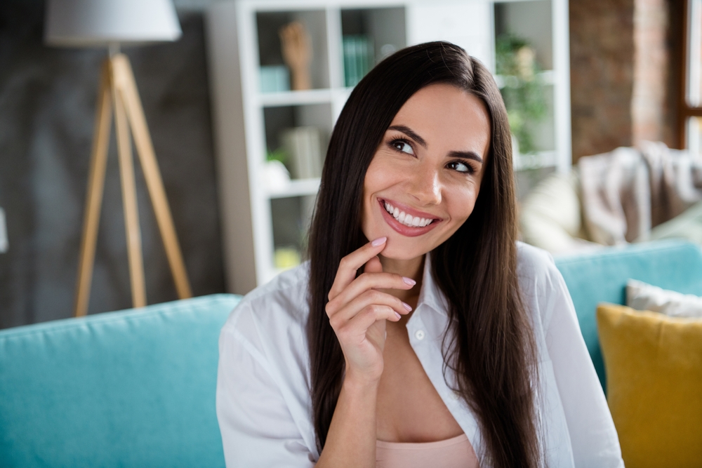 Woman with radiant smile at home after dental treatment – CBCT A happy woman with long dark hair smiles naturally while relaxing indoors, reflecting confidence and beautiful results achieved through precision CBCT-assisted dentistry.