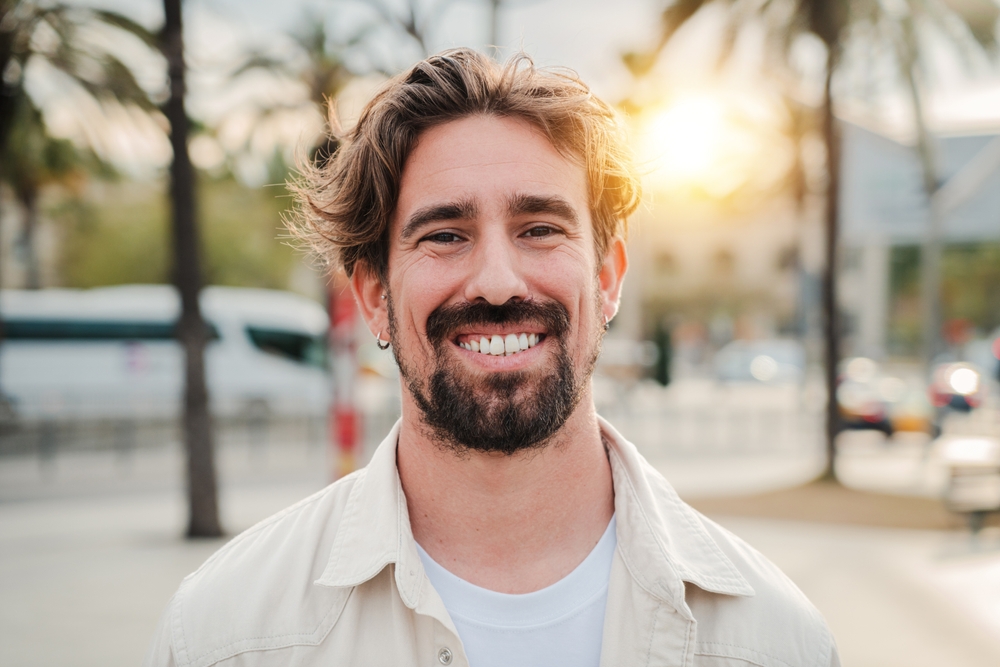 Confident man smiling outdoors in natural light – Diagnosis of Facial and Referred Pain A cheerful man with a beard smiles confidently outdoors at sunset, showing relief and restored comfort – Diagnosis of Facial and Referred Pain.