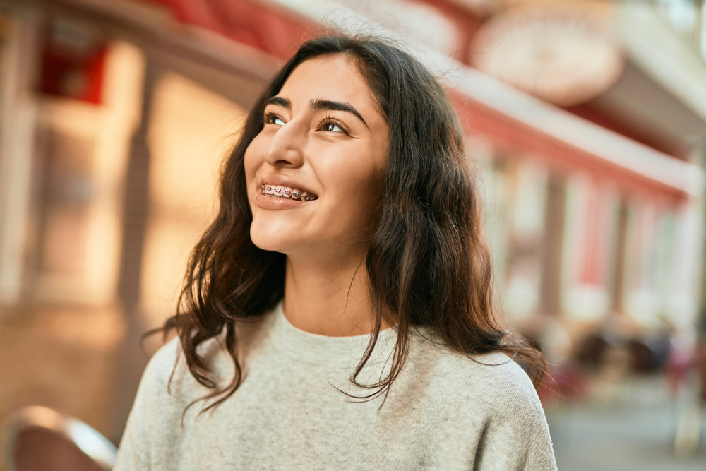 Young woman smiling with braces in sunlight – Diagnosis of Facial and Referred Pain A happy woman with braces enjoys a moment outdoors, her bright smile reflecting confidence and well-being – Diagnosis of Facial and Referred Pain.