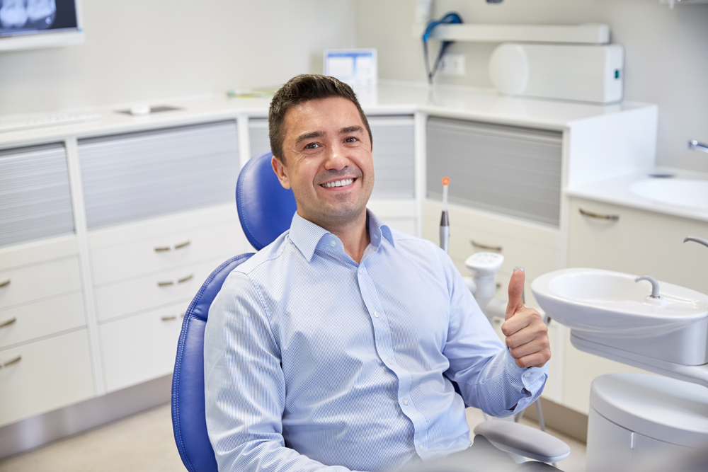 A smiling man sitting in a modern dental chair gives a thumbs up after a successful visit, representing comfort and satisfaction with advanced CBCT diagnostic technology.