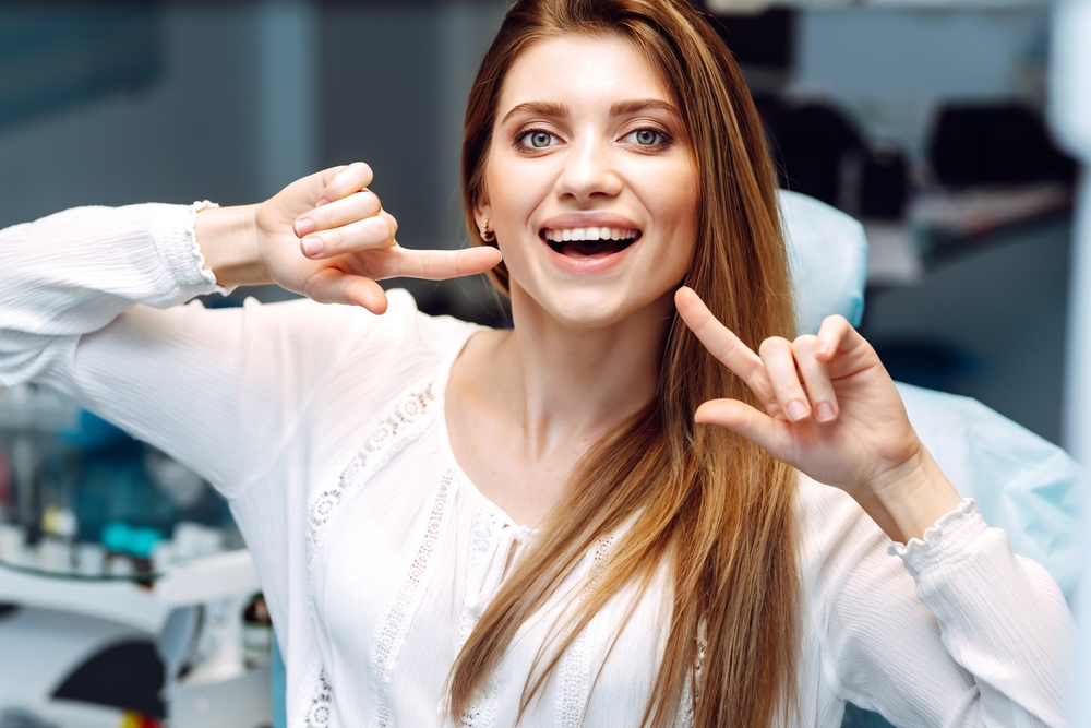 Happy patient showing bright smile at dental clinic – Root Canal Bixby Knolls A joyful woman points to her healthy, white teeth while sitting in a dental chair, showcasing excellent results after treatment – Root Canal Bixby Knolls.